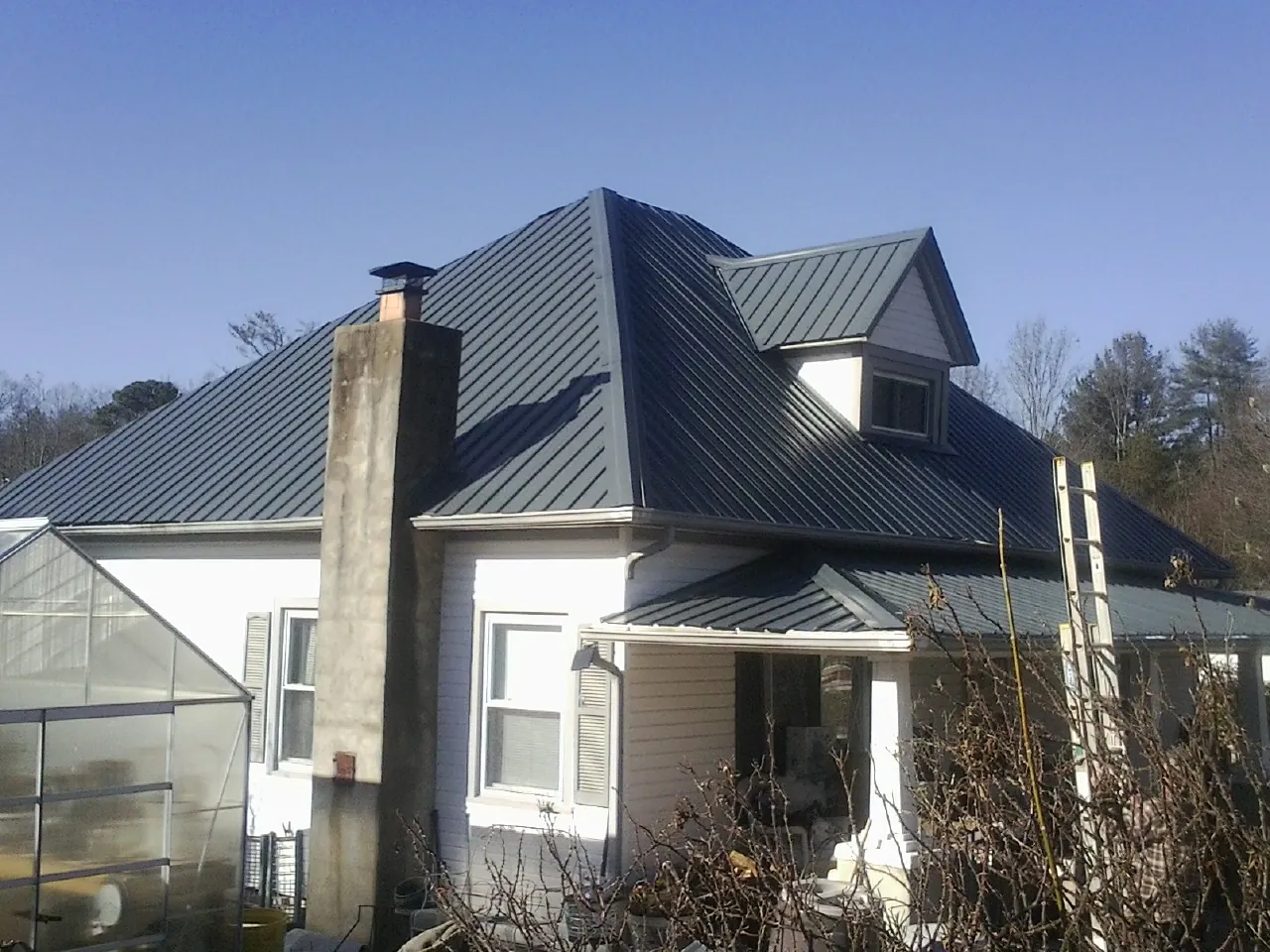 Dark blue standing seam metal roof on a white farmhouse with dormer — Slate & Tile Roof Repair by Roofing Brothers in Elk Creek