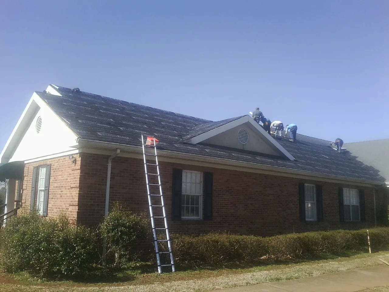 Crew tearing shingles off a brick ranch roof with a ladder set — Metal Roof Repair work by our crew in Elk Creek